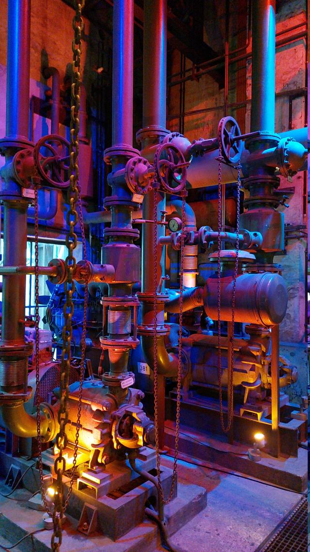 A complex array of industrial pipes and valves bathed in dramatic purple and golden light.