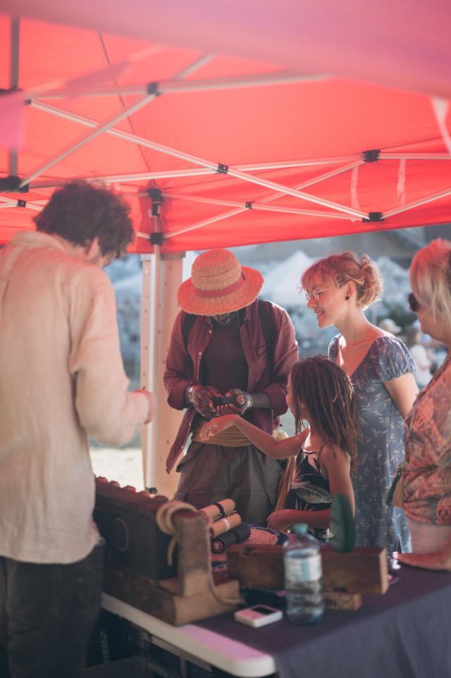 Scene with market visitors and Thomas at the exhibition stand on a sunny day.