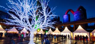 Weihnachtsmarkt bei Nacht mit beleuchtetem Baum und festlich geschmückten Ständen.