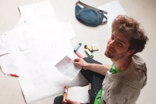 Rollgut Founder Thomas Sommer sitting on the floor, surrounded with papers and writing utensils, engaged in creative work using Rollgut